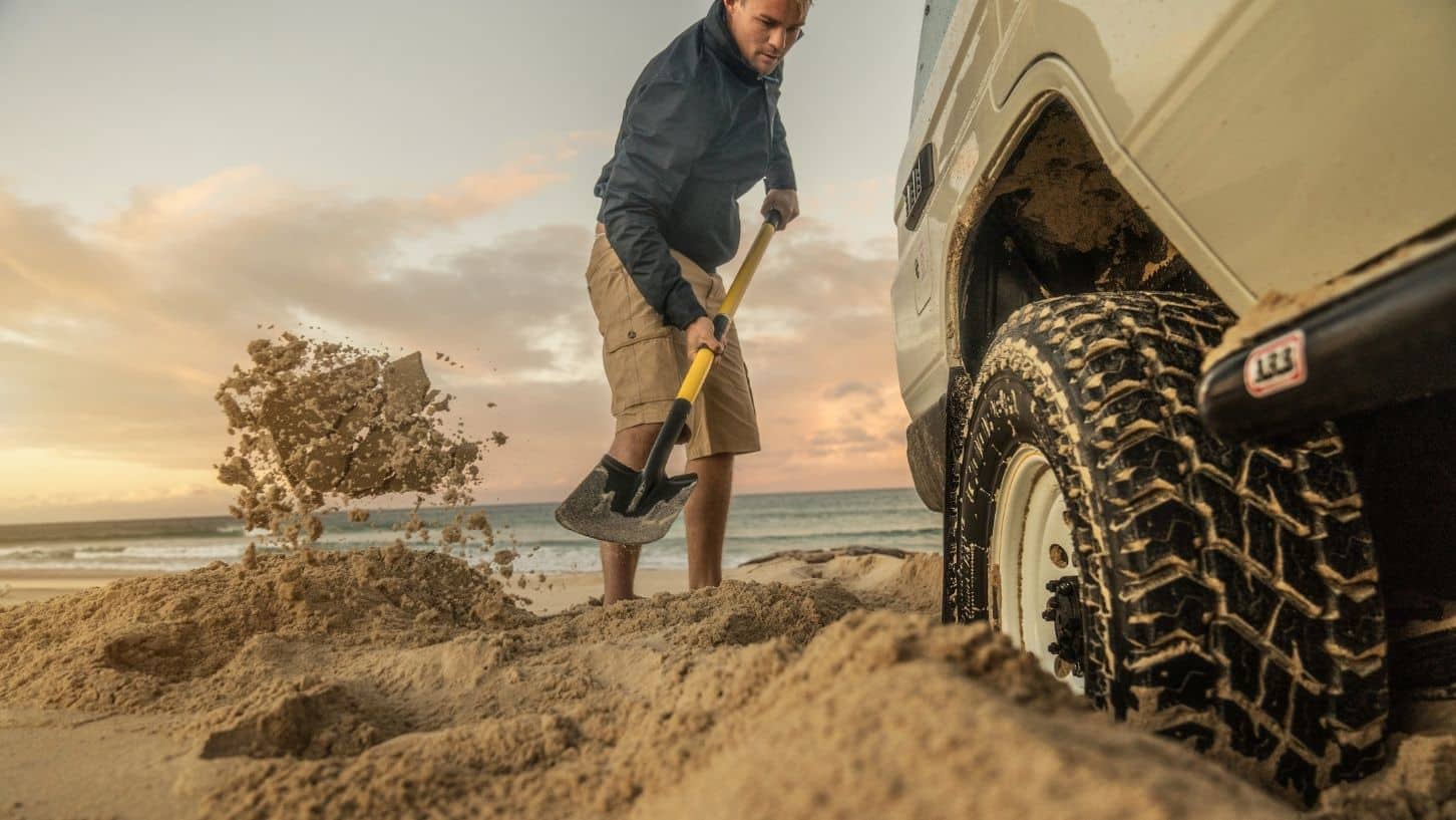 Man digging sand out from under his wheels