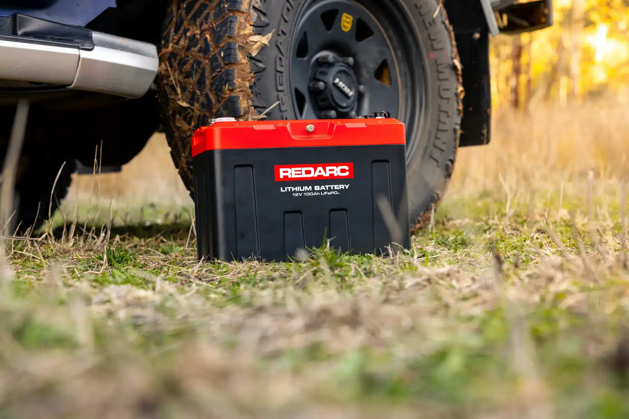 REDARC REDLAB battery positioned next to 4X4 wheel in outdoor setting